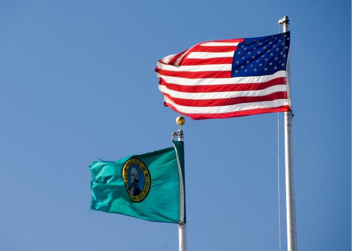 Image of Washington state flag with American flag flying in the blue sky